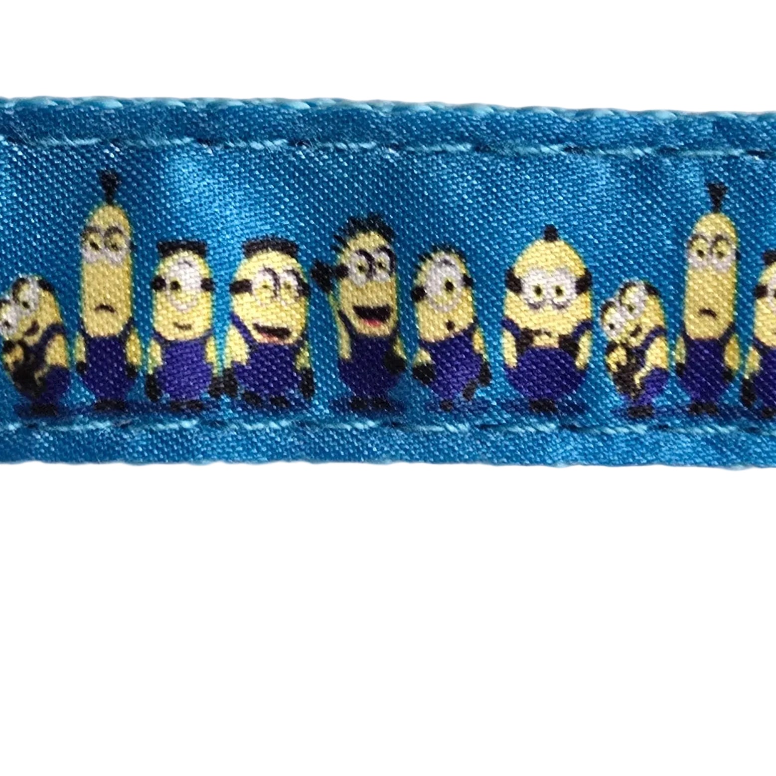 A close-up of a blue fabric trim or ribbon featuring a repeating pattern of cartoon Minions characters, laid horizontally against a textured off-white wall.